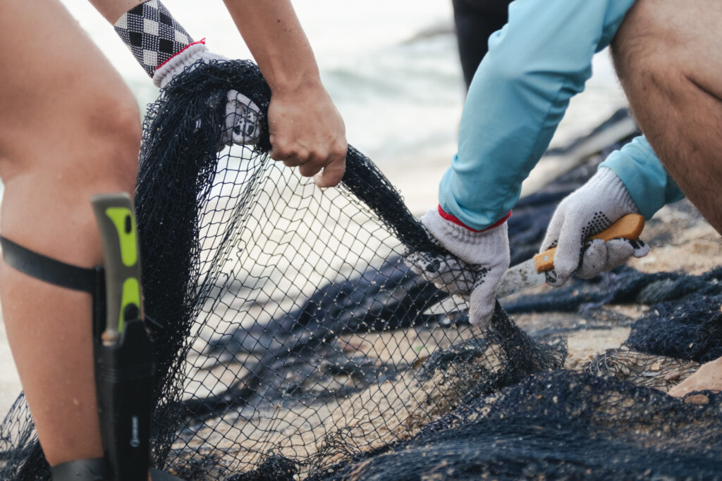 Mãos com luvas retiram uma rede de pesca abandonada da areia da praia